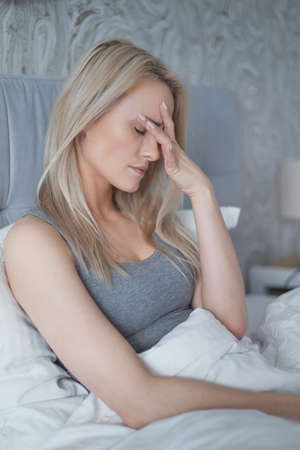 Women sitting on bed holding her head. She has a painful headache with migraine.の写真素材
