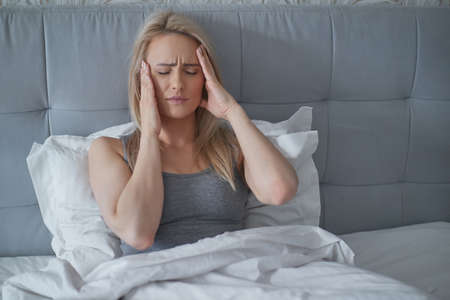 Women sitting on bed holding her head. She has a painful headache with migraine.の写真素材