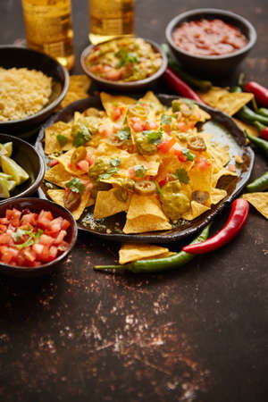 Fresh yellow corn nacho chips garnished with melted cheese, peppers and tomatoes in a handmade ceramic plate on rusty tableの写真素材