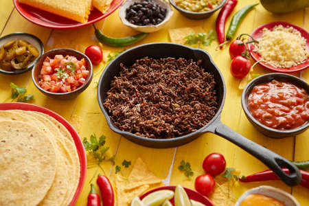 Various fresh and tasty ingredients for chilli con carne. With meat on iron pan, tortillas, vegetables, cheese, bean. Placed on wooden yellow tableの写真素材