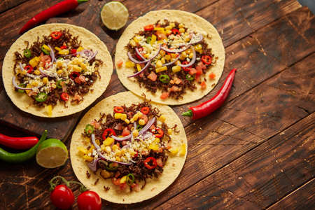Healthy corn tortillas with grilled beef, fresh hot peppers, cheese, tomatoes over rusty wooden table background, top view, copy space. Mexican food contept.の写真素材