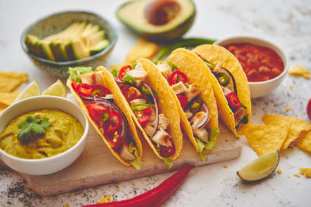 Delicious Mexican fresh crispy tacos are served on wooden board. Stuffed with grilled chicken, spicy pepper, onion, tomato and more. With salsas on side.の写真素材