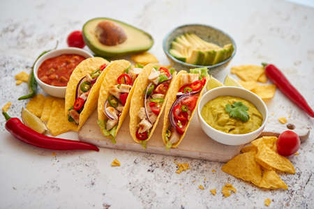 Delicious Mexican fresh crispy tacos are served on wooden board. Stuffed with grilled chicken, spicy pepper, onion, tomato and more. With salsas on side.の写真素材