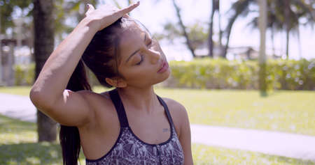 Sportive Asian woman having break and touching head closing eyes in park Thailand, Phuketの写真素材