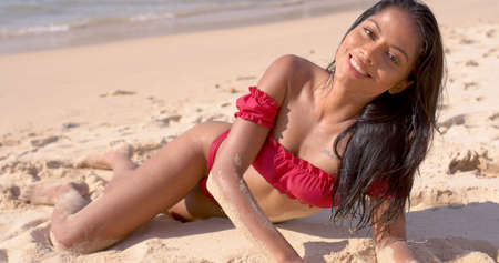 Satisfied Asian female tourist in fashionable pink bikini lying on sandy sea beach and looking at camera at Phuketの写真素材