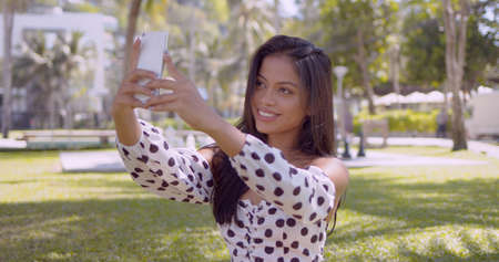 Long haired charming Asian woman in fashion top with open shoulders taking selfie in park in Thailand, Phuketの写真素材
