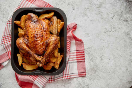 Roasted chicken or turkey with potatoes in black steel mold placed on napkin, flat lay with copy space on stone background. Top view.の写真素材