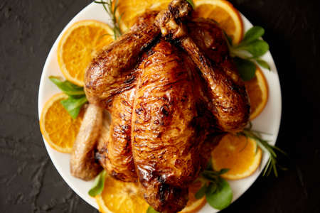 Roasted whole chicken or turkey served in white ceramic plate with oranges and lamb's lettuce on dark stone background. View from above.の写真素材