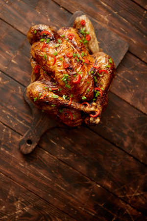 Homemade roasted spicy chicken with chilli and chive. Served on dark brown chopping board. Old wooden background, Shot from above.の写真素材