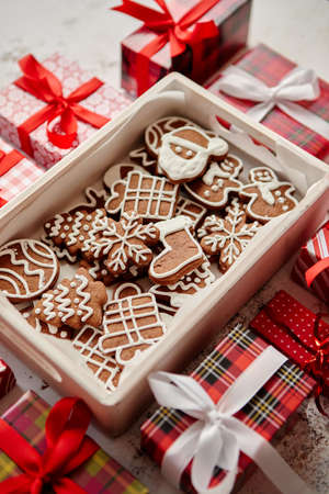 Delicious fresh Christmas decorated gingerbread cookies placed in wooden crate. Wrapped gifts on sides. White rusty background. Top view.の写真素材