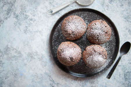 Fresh and tasty chocolate muffins served on plate. Covered with powder sugar. Placed on stone background. Top view with copy spaceの写真素材