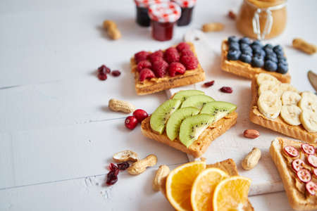 Assortment of healthy fresh breakfast toasts. Bread slices with peanut butter and various fruits and ingredients on side. Placed on white wooden table. Top view, with copy space.の写真素材