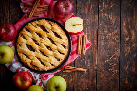 Homemade pastry apple pie with bakery products on dark rusty wooden kitchen table red and green apples and cinnamon. Traditional american dessert. Flat lay food background. Top viewの写真素材
