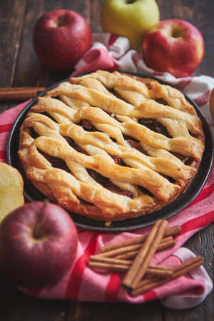 Traditional american apple pie served with fresh fruits, cinnamon sticks in a black ceramic plate. Flat lay and top view on rusty wooden table.の写真素材
