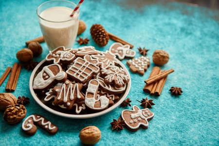 Sweet Christmas composition. Assortment of gingerbread cookies on a plate. Glass of milk, vanilla sticks, anise, pine, walnut. Top view. On blue background.の写真素材