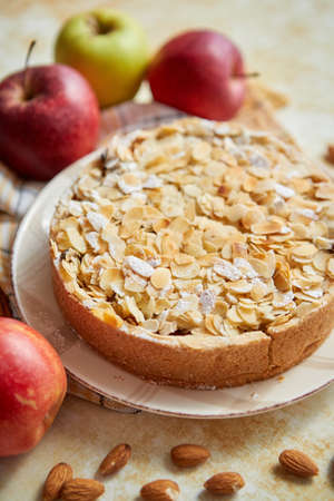 Freshly baked homemade apple pie with almond flakes cake on yellow rusty background. Fresh apple fruits, cinnamon sticks and icing sugar. Top view with copy space.の写真素材