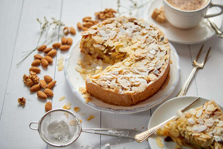 Horizontal shot of a whole round delicious apple cake tart with almond flakes served on wooden table. With coffee in a cup and slice of a pie on soucer.の写真素材