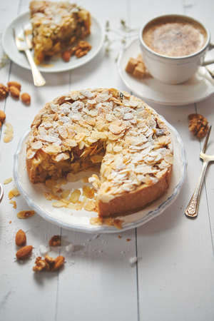 Horizontal shot of a whole round delicious apple cake tart with almond flakes served on wooden table. With coffee in a cup and slice of a pie on soucer.の写真素材