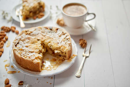 Horizontal shot of a whole round delicious apple cake tart with almond flakes served on wooden table. With coffee in a cup and slice of a pie on soucer.の写真素材