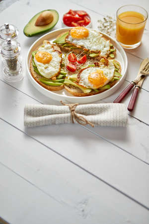 Delicious healthy breakfast with sliced avocado sandwiches with fried egg on top of bread. With orange juice, cherry tomatoes, radish sprouts, salt and peper. Flat lay, top view.の写真素材
