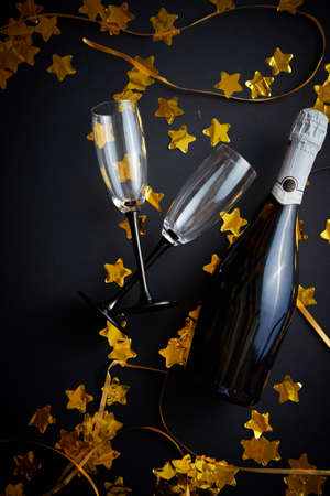 Glasses and bottle of champagne with golden serpentines and confetti lying on black background. New Year or party celebration concept. Top view. Flat lay.の写真素材