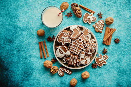 Sweet Christmas composition. Assortment of gingerbread cookies on a plate. Glass of milk, vanilla sticks, anise, pine, walnut. Top view. On blue background.の写真素材