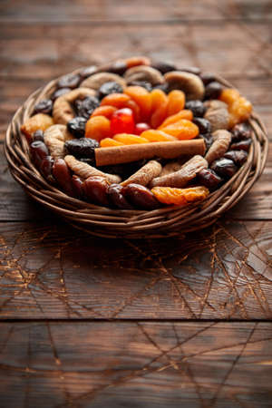 Mix of dried fruits in a small wicker basket on wooden table. Assortment contais apricots, plums, figs, dates, cherries, peaches. Above view with copy space.の写真素材
