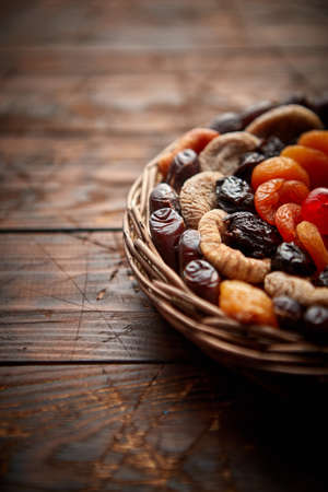Mix of dried fruits in a small wicker basket on wooden table. Assortment contais apricots, plums, figs, dates, cherries, peaches. Above view with copy space.の写真素材