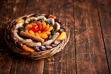 Mix of dried fruits in a small wicker basket on wooden table. Assortment contais apricots, plums, figs, dates, cherries, peaches. Above view with copy space.の写真素材