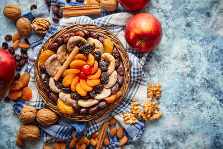 Composition of dried fruits and nuts in small wicker bowl placed on a stone table. Assortment contais almonds, walnuts, apricots, plums, figs, dates, cherries, peaches. Above view with copy space.の写真素材
