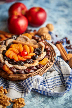 Composition of dried fruits and nuts in small wicker bowl placed on a stone table. Assortment contais almonds, walnuts, apricots, plums, figs, dates, cherries, peaches. Above view with copy space.の写真素材