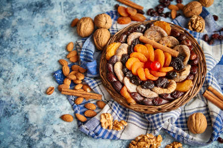 Composition of dried fruits and nuts in small wicker bowl placed on a stone table. Assortment contais almonds, walnuts, apricots, plums, figs, dates, cherries, peaches. Above view with copy space.の写真素材