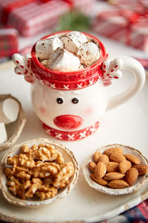 Delicious homemade christmas hot chocolate or cocoa with marshmellows in a red xmas decorative cup. With almonds, walnuts in small bowls on sideの写真素材