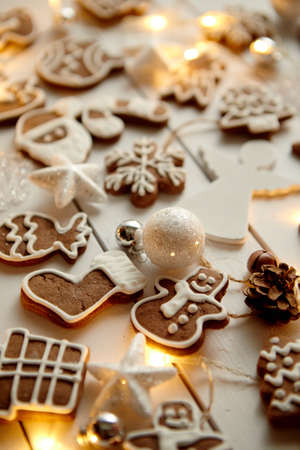 Christmas sweets composition. Gingerbread various shaped cookies with xmas decorations arranged on white wooden table with lights.の写真素材