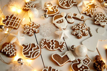 Christmas sweets composition. Gingerbread various shaped cookies with xmas decorations arranged on white wooden table with lights.の写真素材