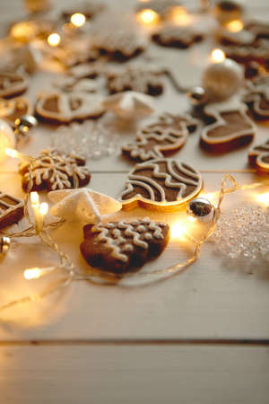 Christmas sweets composition. Gingerbread various shaped cookies with xmas decorations arranged on white wooden table with lights.の写真素材