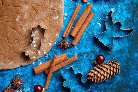 Christmas baking concept. Gingerbread dough with different cutter shapes and spices on sides. Top view on blue rustic background.の写真素材