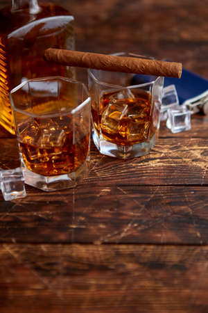 Bottle of whiskey with two glasses and cuban cigar placed on rustic wooden table.の写真素材