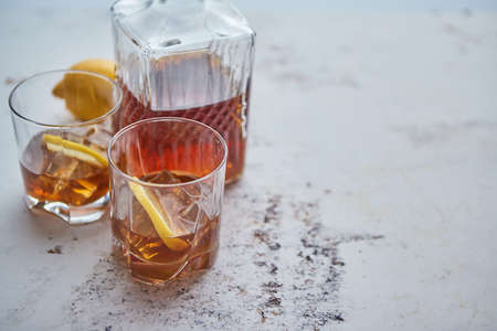Whiskey sour drink with lemon in glass on stone rustical background. Two glasses filled with ice and carafeの写真素材