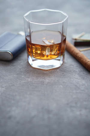 Glass of whiskey with ice, big cuban cigar, matches and hip flask placed on gray stone table.の写真素材