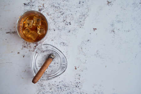Whiskey or brandy in a glass with Cuban cigar on an gray stone table. With ice cubesの写真素材