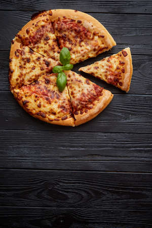 Sliced pizza Margarita with basil leafs placed on black wooden table, top viewの写真素材