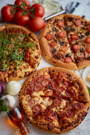 Three american style pizzas with thin fluffy dough served on a table. Placed with various ingredients on side.の写真素材