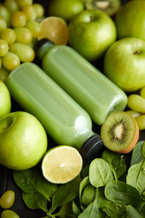 Fresh fruits and vegetables in green color concept. Placed with bottles of smoothie or juice on black wooden table.の写真素材