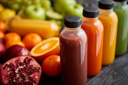 Colorful bottles filled with fresh fruit and vegetable juice or smoothie. Placed in row on black wooden table.の写真素材