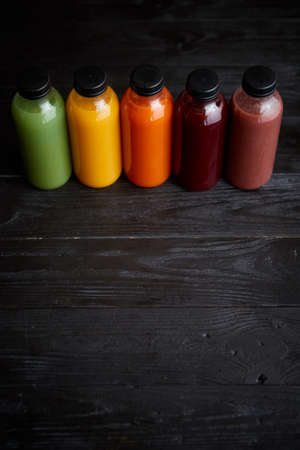 Colorful bottles filled with fresh fruit and vegetable juice or smoothie. Placed in row on black...