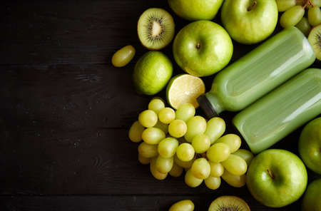 Mixed green fruits and vegetables placed on black wooden table. With botteled juice or smoothie. Healthy diet concept.の写真素材