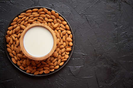 Composition of almonds seeds and milk, placed on black stone background. Copy space for text.