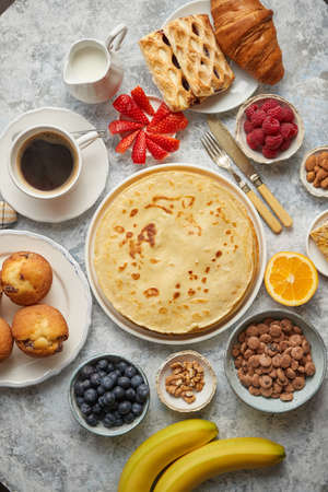 Various breakfast ingredients placed on stone table. With pancakes, muffins, fresh fruits, cupcakes, black coffee in cup. Flat lay. View from above.の写真素材