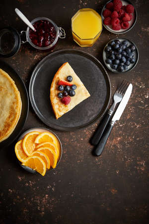 Tasety homemade pancake on black ceramic plate. Placed on dark rusty table. With fresh fruits, orange juice and marmalade. Top view, Flat lay.の写真素材